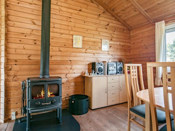 L’intérieur d’une cabane en bois, avec un poêle à bois, un meuble contenant des haut-parleurs et une table à manger avec des chaises.