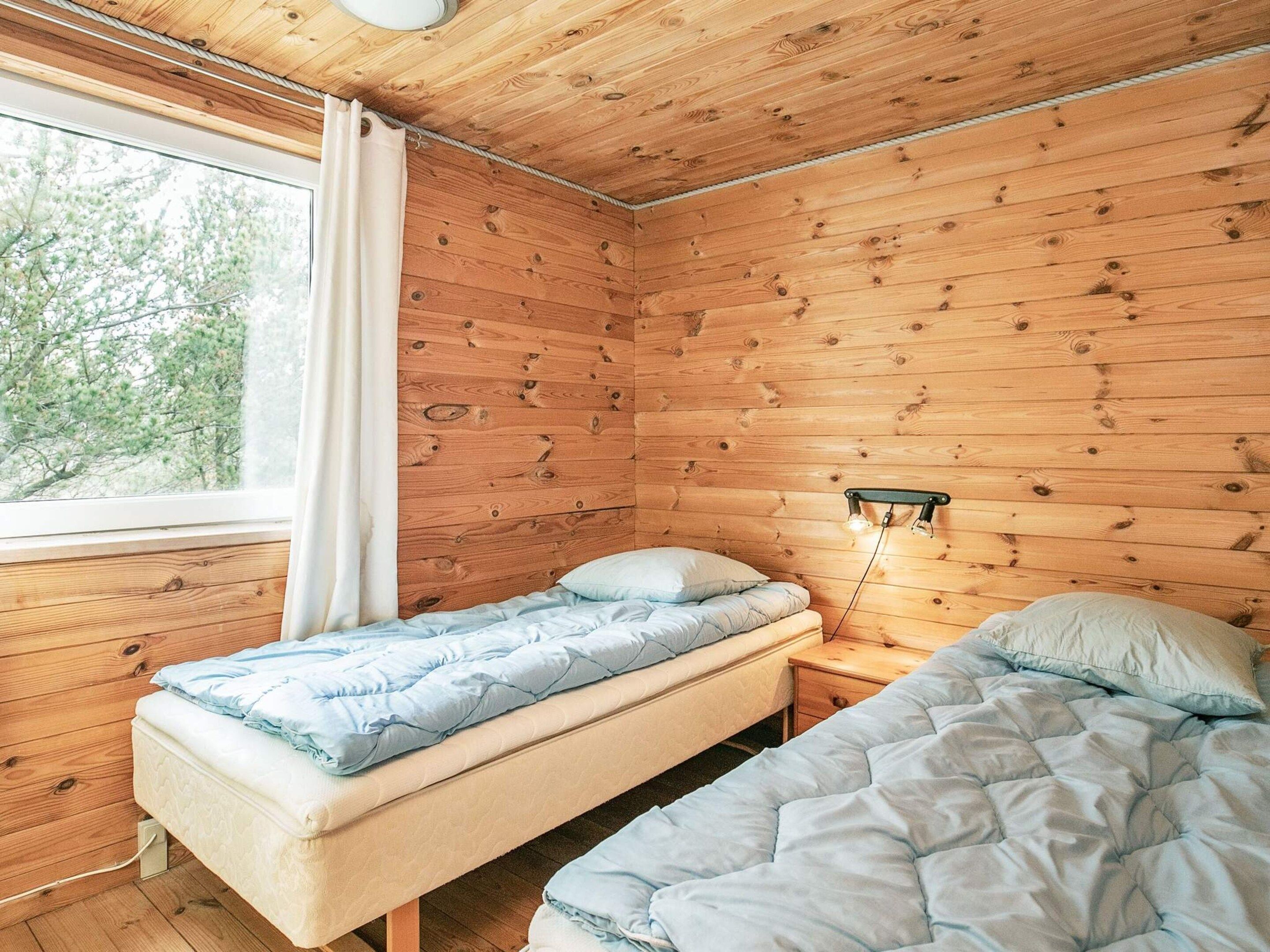 Een kamer met een hutgevoel, met twee bedden, een raam met gordijnen en een wandlamp.