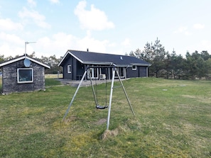 A house with a porch and a swing set in a grassy yard.