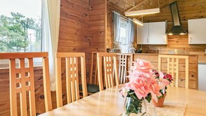 Un intérieur en bois comprenant une table à manger, des chaises, un vase avec des fleurs et un coin cuisine.