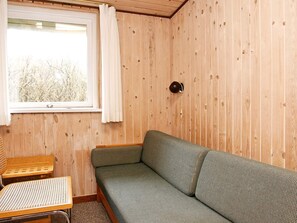 Una habitación con pared de madera, ventana con cortina, un sofá y una pequeña mesa.