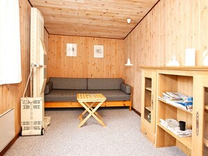 Una habitación pequeña y acogedora con techo de madera, un sofá, una mesita y un armario con estantes.