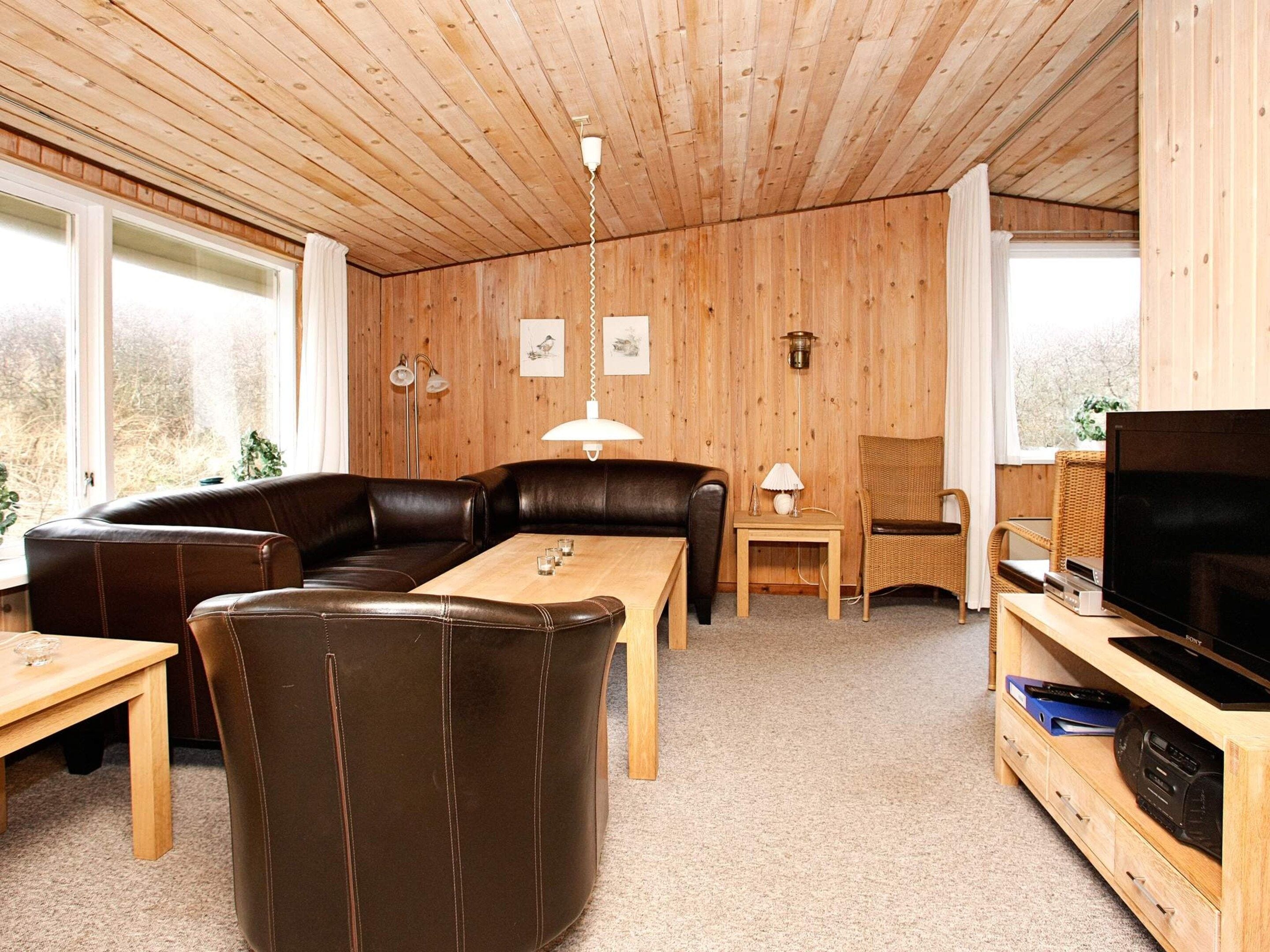 A wooden-paneled room with a sofa, a dining table, a television, and a lamp.