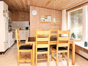 A wooden interior with a dining table and chairs, a kitchen area, and a window with a view.