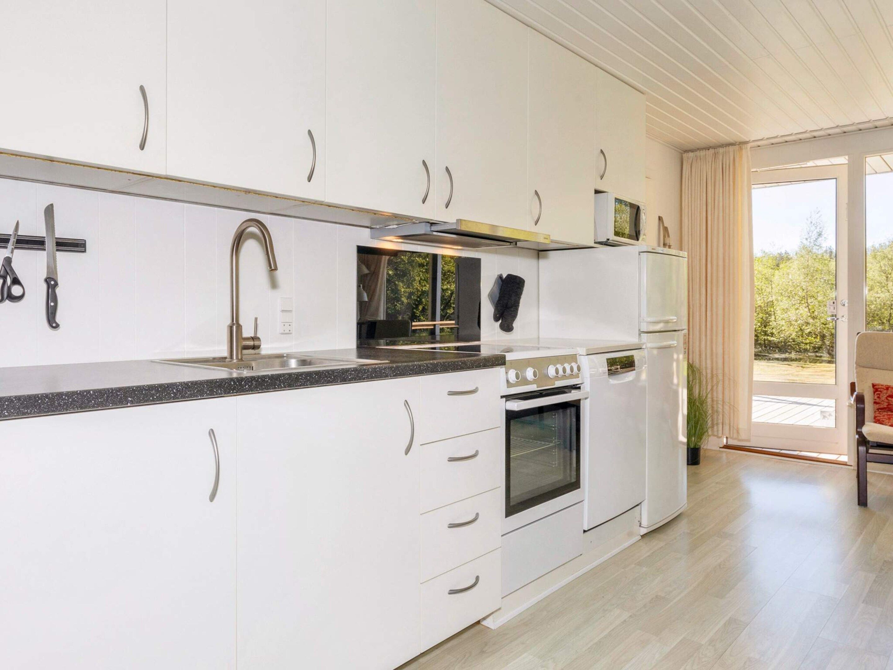A modern kitchen with white cabinets, a stainless steel sink, and a built-in oven.