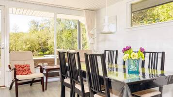 A dining area with a glass table, six chairs, and a vase with flowers.