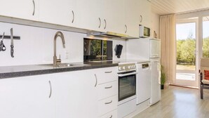 Una cuina moderna amb armaris blancs, electrodomèstics d'acer inoxidable i un gran finestral que ofereix vistes a l'exterior.