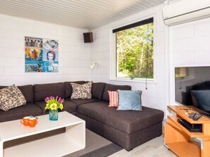 A modern living room with a sectional sofa, a coffee table, a TV stand, and a large window with a view of trees. - 4 Star Holiday Home in Fur (Fur)