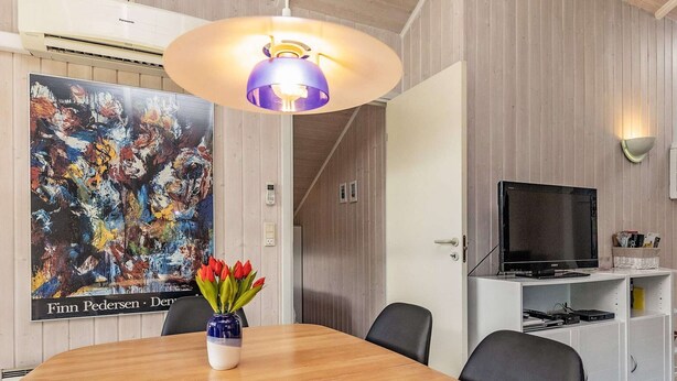 Ein modernes Zimmer mit einem Holztisch, einer Vase mit roten Tulpen, einer blau-weißen Schüssel, einem Sony-Fernseher auf einem weißen Schrank und einem großen abstrakten Gemälde an der Wand.