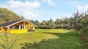 Ein gelbes Haus mit geneigtem Dach, umgeben von einem Rasen und Bäumen.
