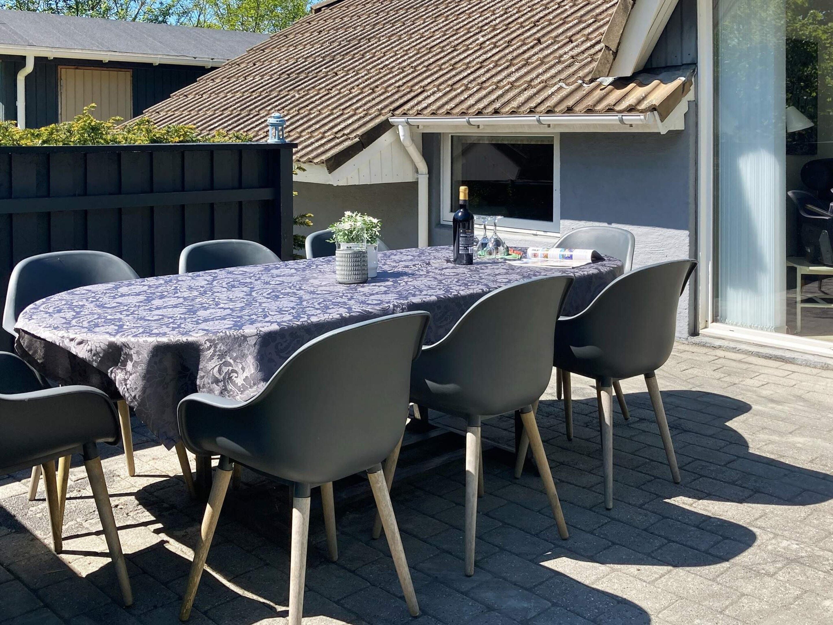 An outdoor patio with a table and chairs, a potted plant, and a bottle of wine.