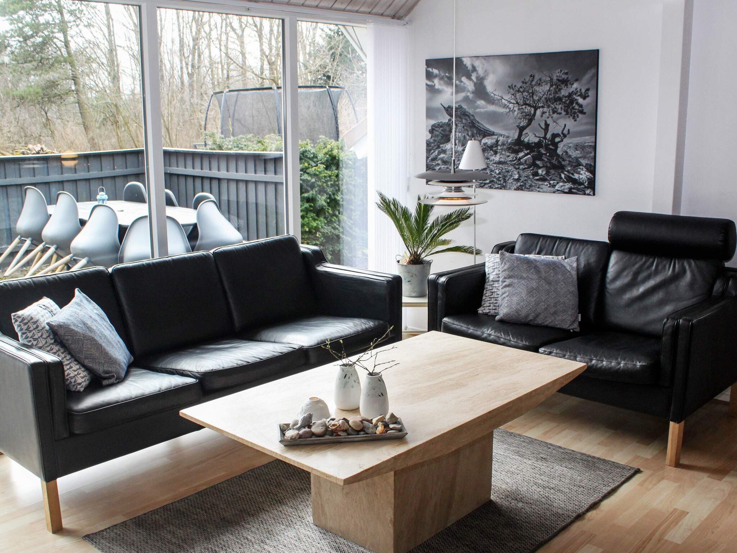 A modern living room with two black leather sofas, a wooden coffee table, and a large window overlooking a deck.
