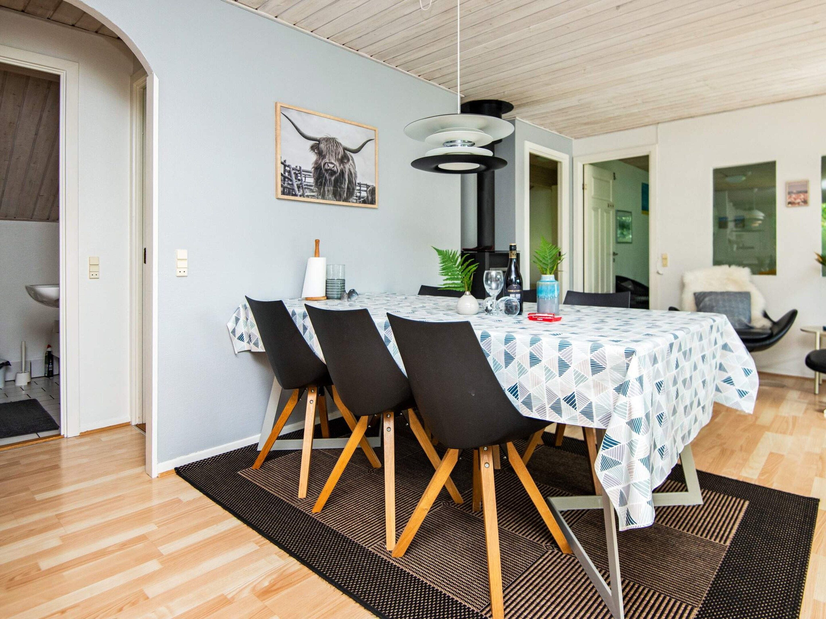 A dining area with a round table, black chairs, a patterned tablecloth, and a pendant light.