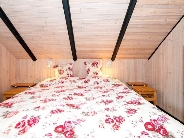 Cozy cabin with a bed, nightstands, and wall-mounted lamps, set amidst a rustic interior with wooden beams and panelled walls.