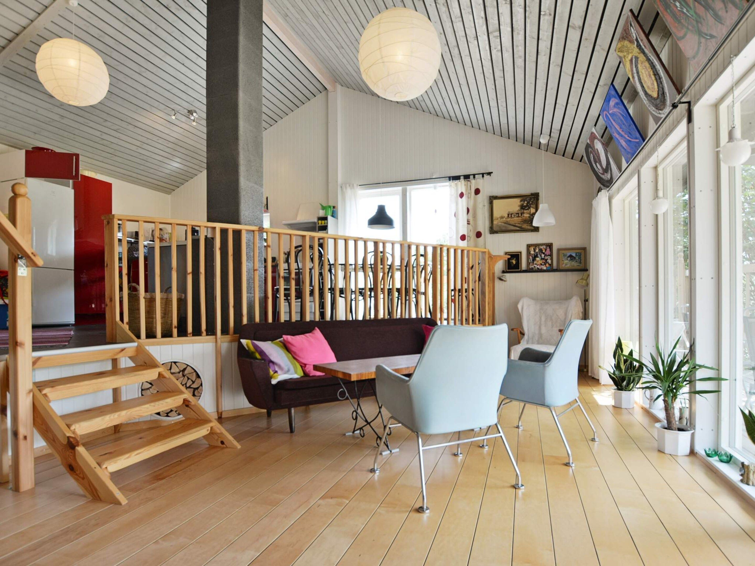 Un amplio espacio habitable con una escalera de madera, un sofá, dos sillones y una mesa de comedor.