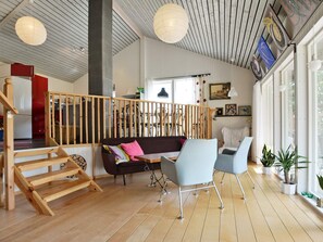 Tilava olohuone, jossa on puinen portaikko, sohva, kaksi nojatuolia ja ruokapöytä.