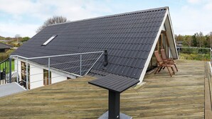 Una casa moderna amb teulada inclinada, terrassa de fusta i un panell solar.
