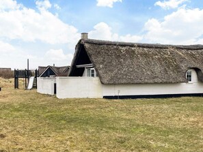 A traditional thatched-roof house with a white exterior, a small window, and a chimney.