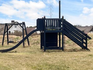 A playground with a slide and swings in a grassy field.