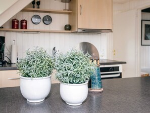 Et køkken med to hvide plantekrukker på bordet, en blå keramisk potte og træskabe med et ur og røde beholdere på hylden.