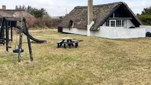 A thatched-roof house with a chimney, a swing set, and a picnic table in a grassy yard.