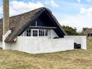 Uma casa moderna com telhado de palha, paredes externas brancas e uma janela grande.