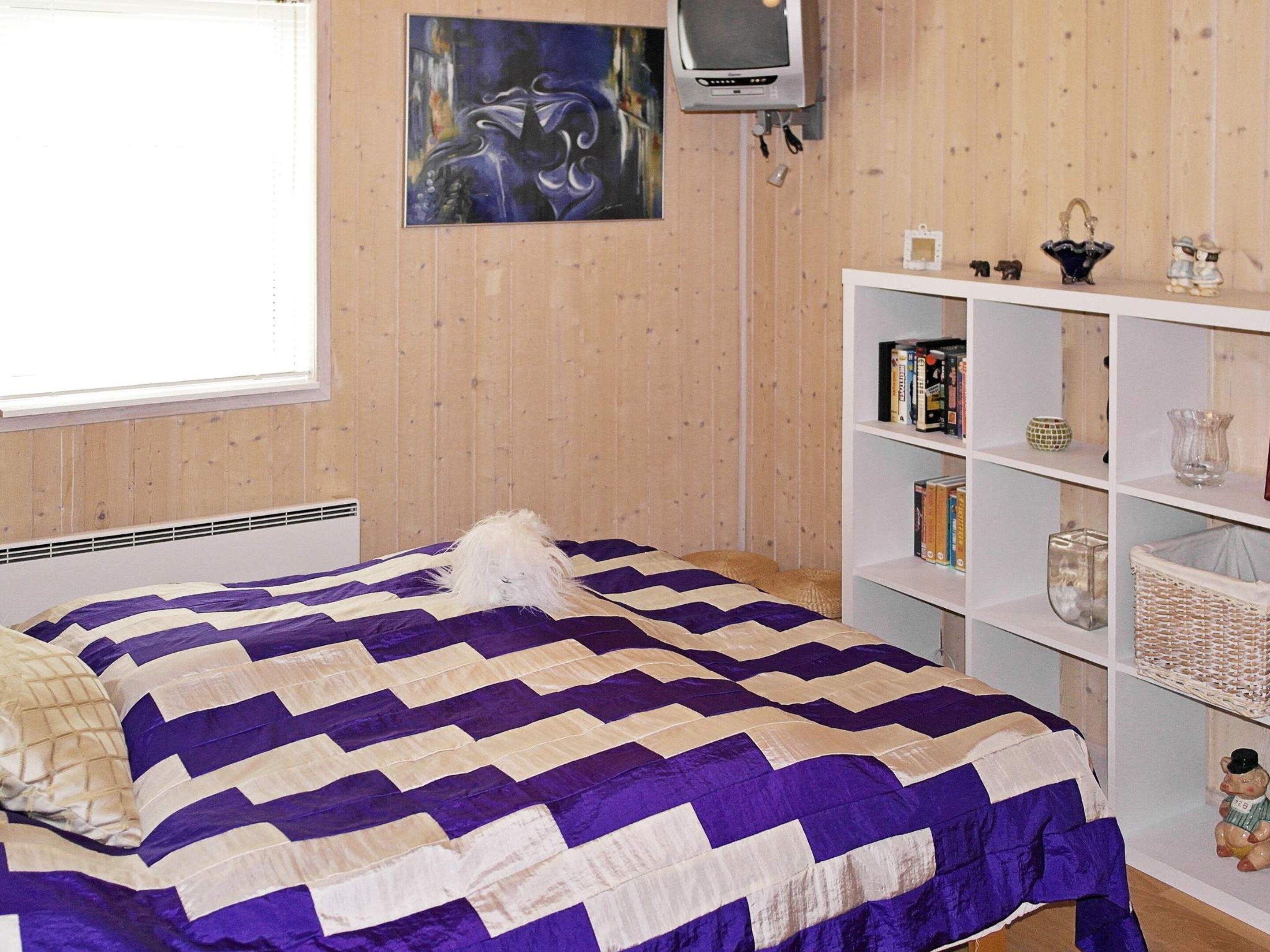 A bedroom with a bed, a bookshelf, a television, and a window.