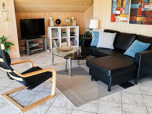 Ett vardagsrum med en svart lädersoffa, ett soffbord i glas, en svart läderfåtölj, en tv, en bokhylla och ett konstverk på väggen.