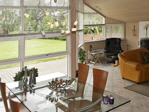 A modern living room with a glass dining table, leather sofa, and large windows offering a view of the outdoors.