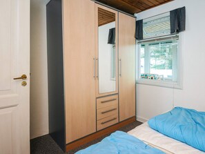 Ein Schlafzimmer mit Kleiderschrank, einem Bett mit blauer Bettwäsche, einem Fenster mit Vorhängen und Blick nach draußen.