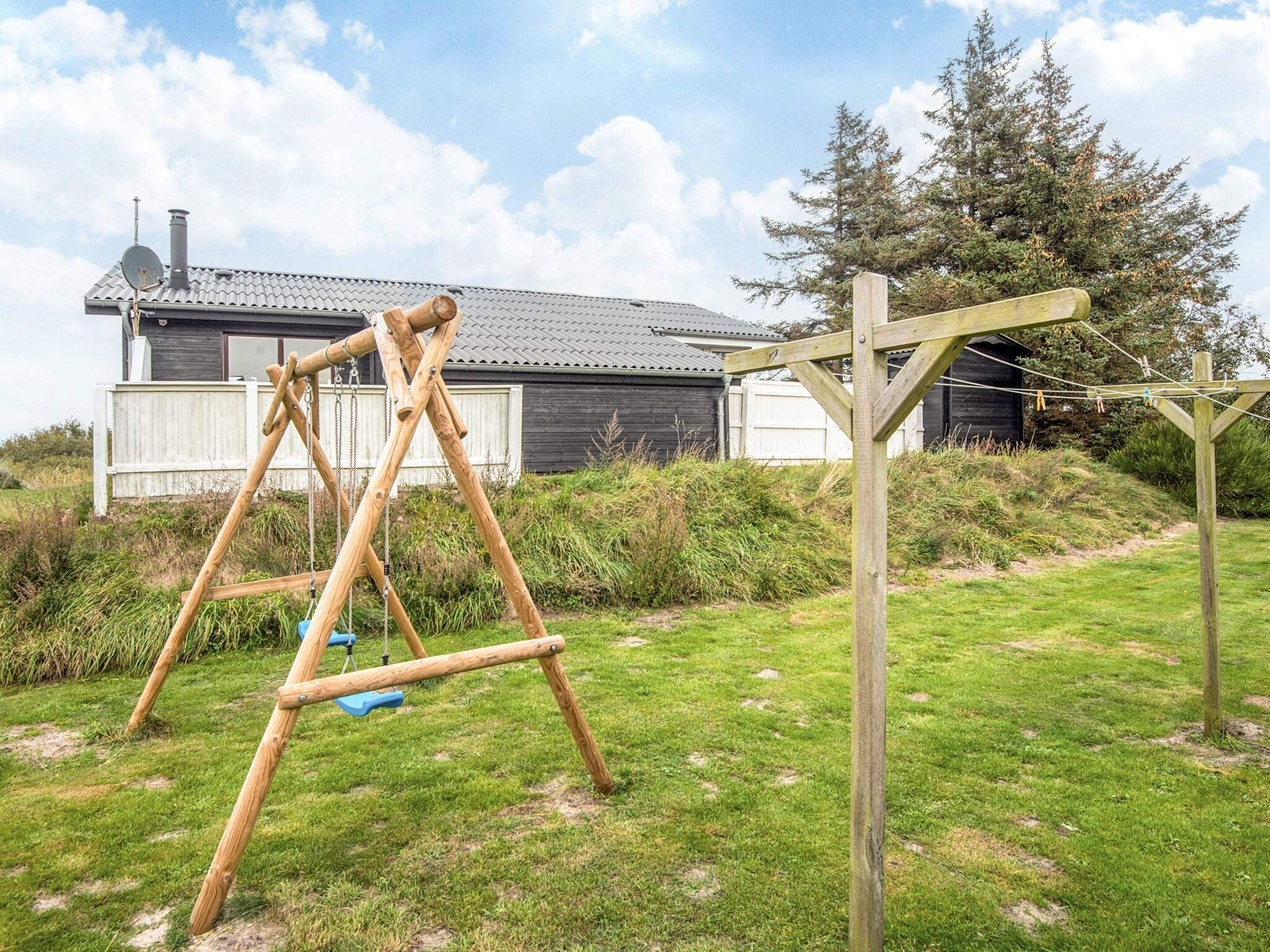 A wooden swing set in a grassy yard with a house in the background.