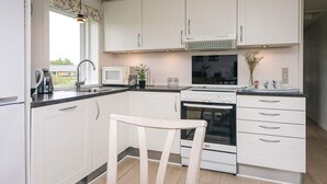A modern kitchen with white cabinets, a microwave, an oven, and a sink. - Cozy Holiday Home in Rømø near Beach (Rømø)