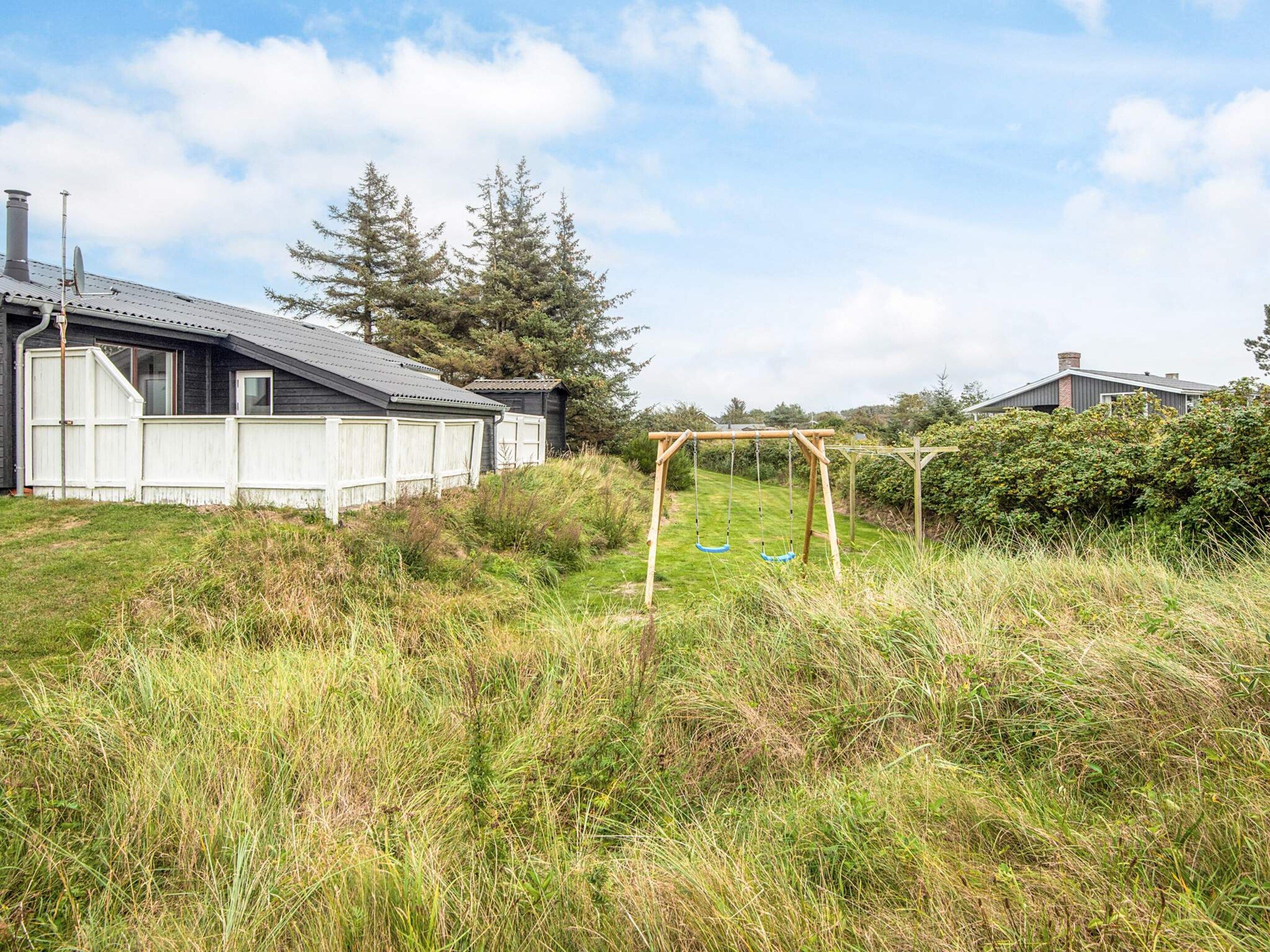 A residential property with a fenced yard, a wooden swing set, and a house with a grey roof.