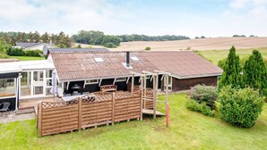 A rustic barn with a sloped roof, a covered outdoor seating area, and a fenced-in space with a grill.