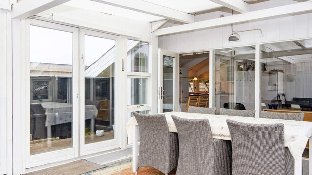 A conservatory with a dining table and chairs, large glass doors, and a view of the outside.