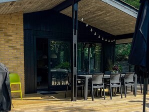 An outdoor patio with a table and chairs, a green chair, and a covered area with a wooden ceiling. - 6 Person Holiday Home in Vaeggerlose-by Traum (Vaeggerlose)