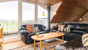 Moderni loft-tyylinen asunto, jossa on puinen kattopaneeli, mustat nahkasohvat, puinen sohvapöytä ja suuret ikkunat.