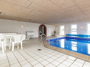 An indoor swimming pool with a tiled floor, a white table with chairs, a ceiling fan, and a brick archway leading to another room. - 5 Star Holiday Home in Fur (Fur)