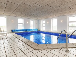 An indoor swimming pool with clear blue water, a tiled floor, and a seating area with blue cushions. - 5 Star Holiday Home in Fur (Fur)