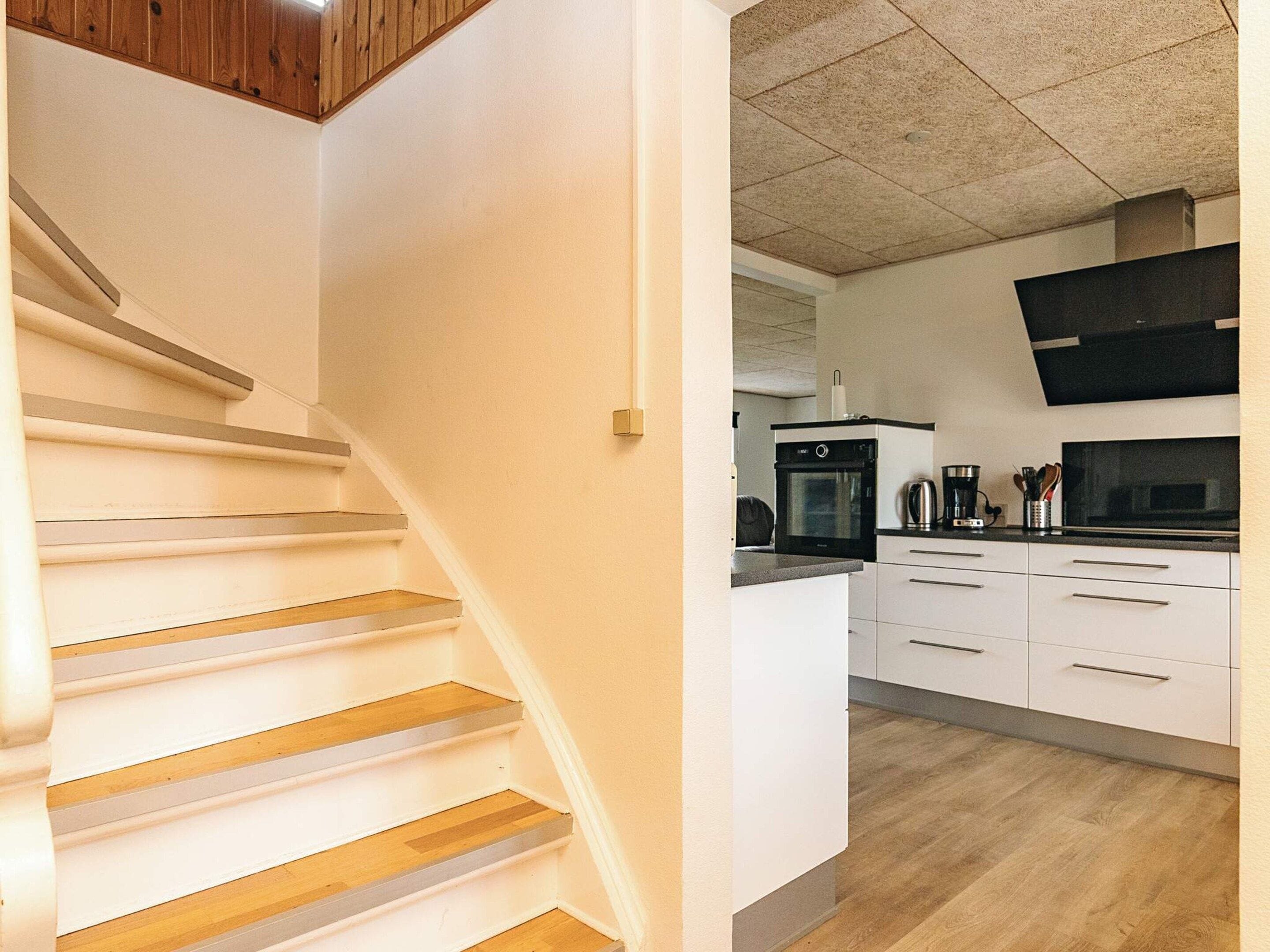 A staircase with wooden steps and white walls leading to a kitchen area with white cabinets, a black oven, and a microwave.