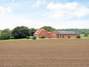 A red brick building with a sloped roof and solar panels, surrounded by a plowed field and trees. - 5 Star Holiday Home in Fur (Fur)