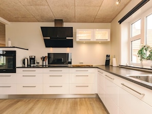 A modern kitchen with a built-in oven, microwave, and coffee maker, white cabinetry, and a large window. - 5 Star Holiday Home in Fur (Fur)