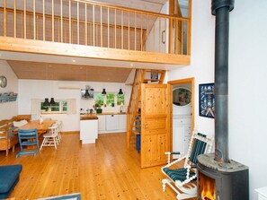 A spacious loft with a wooden staircase, a kitchen with white cabinets, a dining area with wooden furniture, and a wood-burning stove. - 8 Person Holiday Home in Jaegerspris-by Traum (Jægerspris)