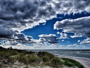 A beach with a grassy foreground and a view of the ocean under a partly cloudy sky.