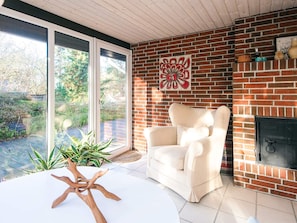 A modern living room with a brick fireplace, a white armchair, and a large window overlooking a garden.