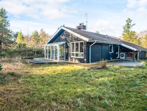 A modern house with a large glass conservatory, a covered outdoor kitchen, and a well-maintained lawn.