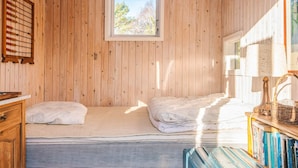 Una habitación acogedora con paredes de madera, una cama con sábanas blancas, un ventanal pequeño y una estantería con libros.