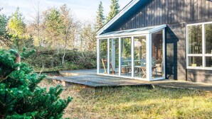 Una casa moderna con un porche de cristal y una terraza de madera.