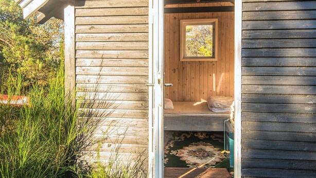 Una pequeña cabaña de madera con una cama, un ventanal y una puerta.