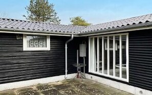 Un bâtiment noir avec un toit recouvert de tuiles, une fenêtre et une porte.